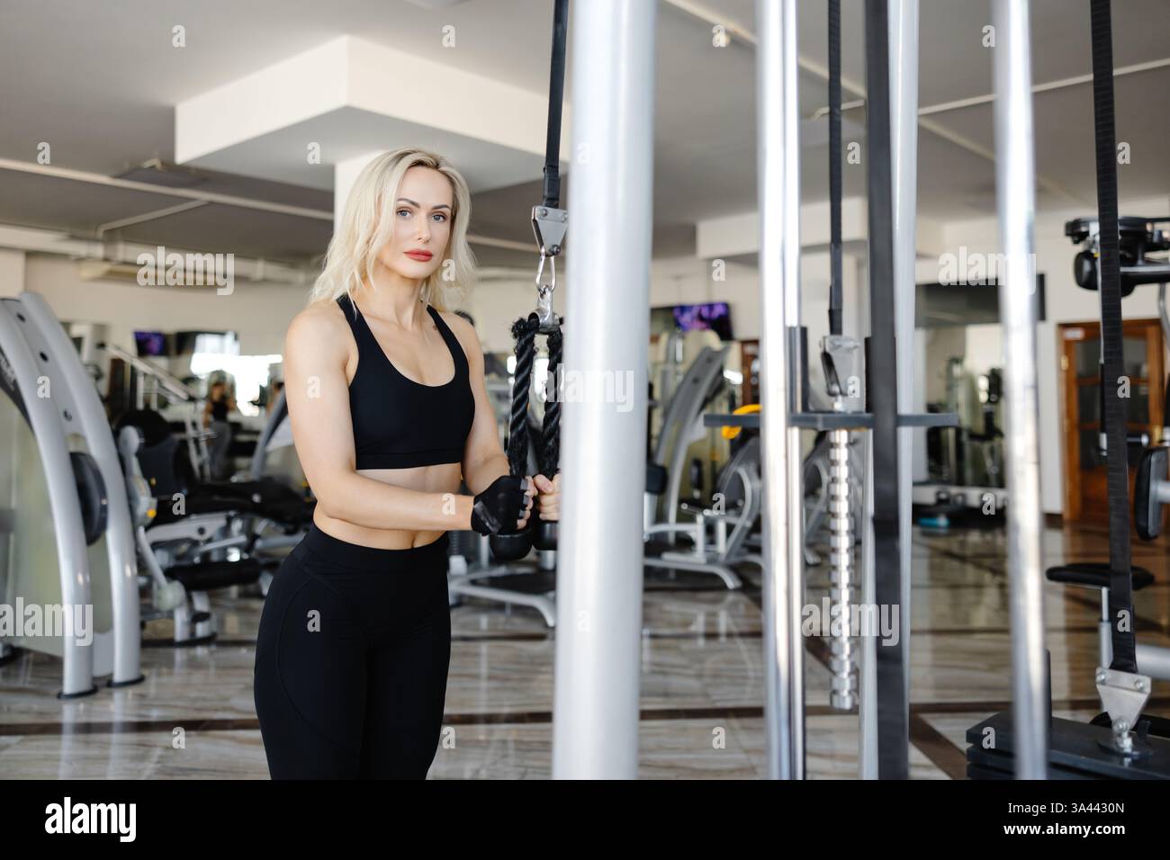 Atleta concentrato che esegue esercizi alla schiena utilizzando una macchina crossover via cavo nel moderno centro fitness, concentrandosi sulla costruzione della forza e sulla definizione dei muscoli Foto Stock