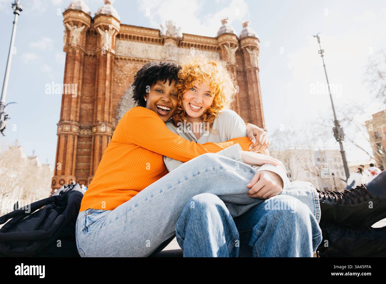 Due donne felici che abbracciano di fronte all'Arc de triomf a barcellona, spagna, godendosi la loro vacanza insieme Foto Stock