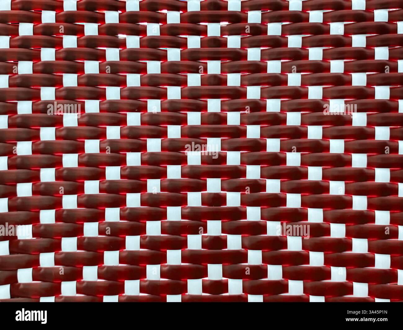 Primo piano del rattan sintetico rosso e bianco o dell'arte della tessitura in vimini con motivo a strisce verticali. Sfondo in rattan intrecciato a mano senza cuciture. Foto Stock
