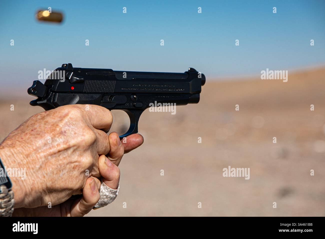 Un involucro esaurito viene espulso mentre un uomo spara una pistola semi-automatica nera. Foto Stock