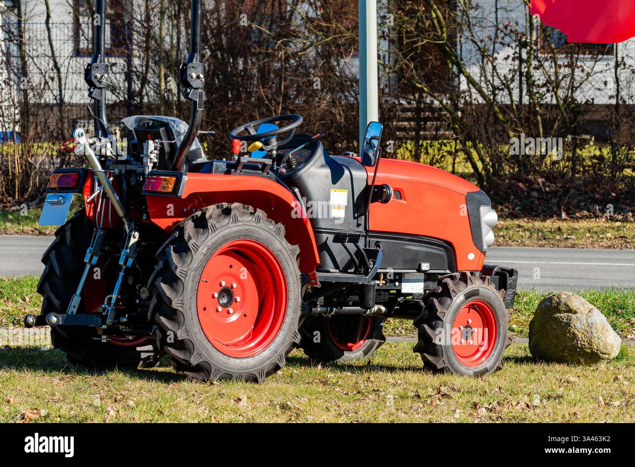 Un trattore rosso vivace è parcheggiato su un'area erbosa accanto a una strada. Presenta ruote di rilievo e un robusto telaio che ne mostra la praticità agricola Foto Stock