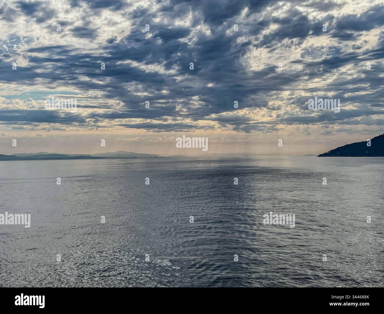 Un vasto orizzonte oceanico si estende sotto un cielo strutturato, con una costa lontana visibile. La superficie d'acqua riflettente e le nuvole a strati creano una penna Foto Stock Un vasto orizzonte oceanico si estende sotto un cielo strutturato, con una costa lontana visibile. La superficie d'acqua riflettente e le nuvole a strati creano una penna Foto Stock
