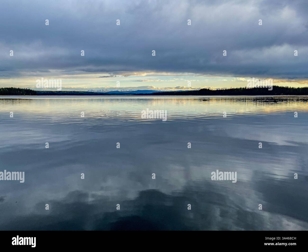 Un lago fermo che riflette il cielo e la catena montuosa lontana al tramonto, con colori tenui e acqua limpida. La tranquilla scena mette in risalto il tranquillo har Foto Stock
