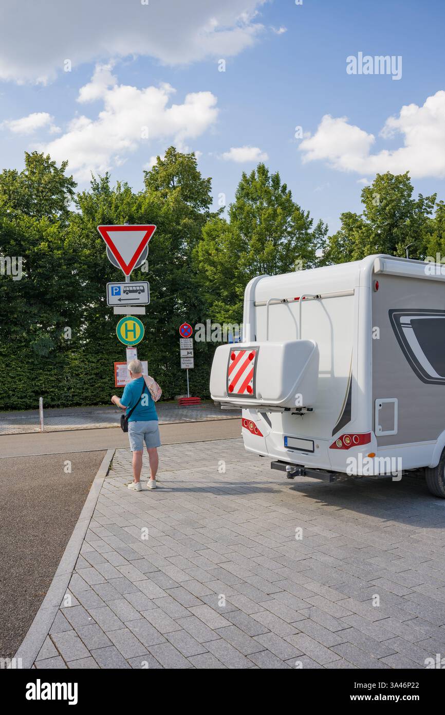 Un uomo è in piedi accanto a un camper. Un viaggiatore si è fermato in un parcheggio per chiarire il percorso. Foto Stock