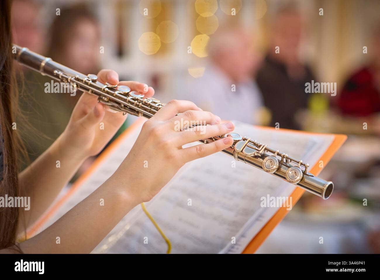 Immagine ravvicinata di un suonatore di flauto immerso in una performance durante una riunione sociale. Le mani tengono delicatamente il flauto su uno spartito aperto, la creatina Foto Stock