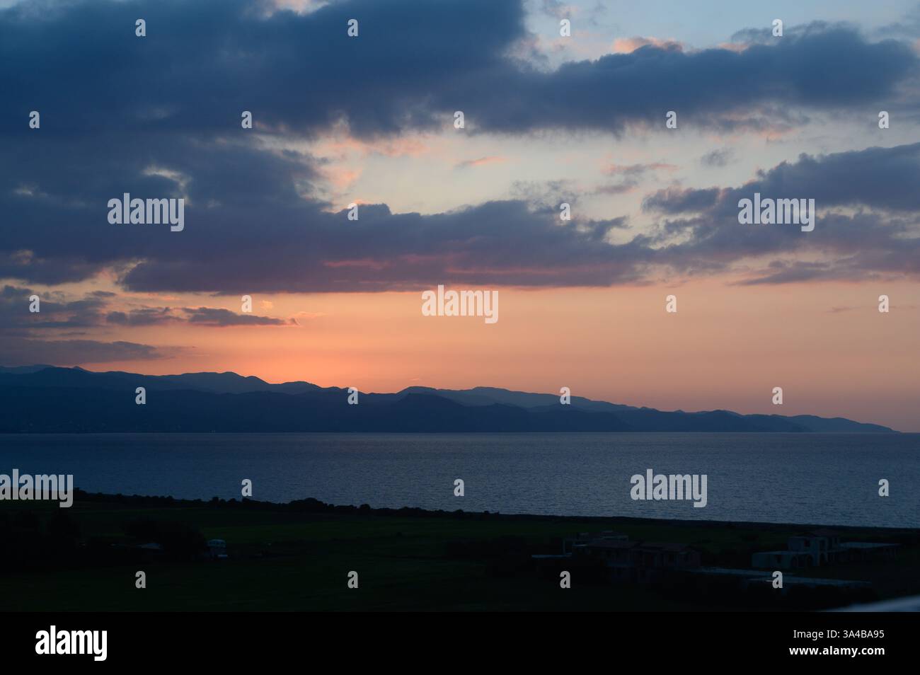 I colori vivaci si fondono nel cielo al tramonto, diffondendo incantevoli riflessi sul mare calmo. Le ombre delle montagne creano uno sfondo sereno, catturando la bellezza Foto Stock