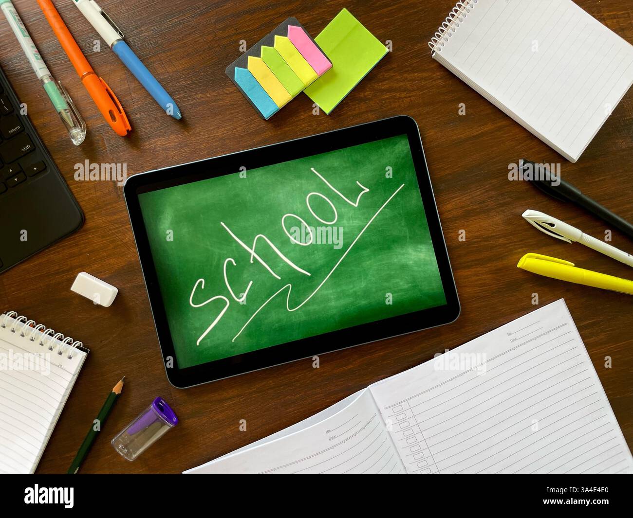 Sul tavolo di legno sono presenti materiali scolastici come un notebook, un blocco note, una penna, una matita, adesivi e una tavoletta. Formazione online moderna. - Immagine stock catturata con smartphone