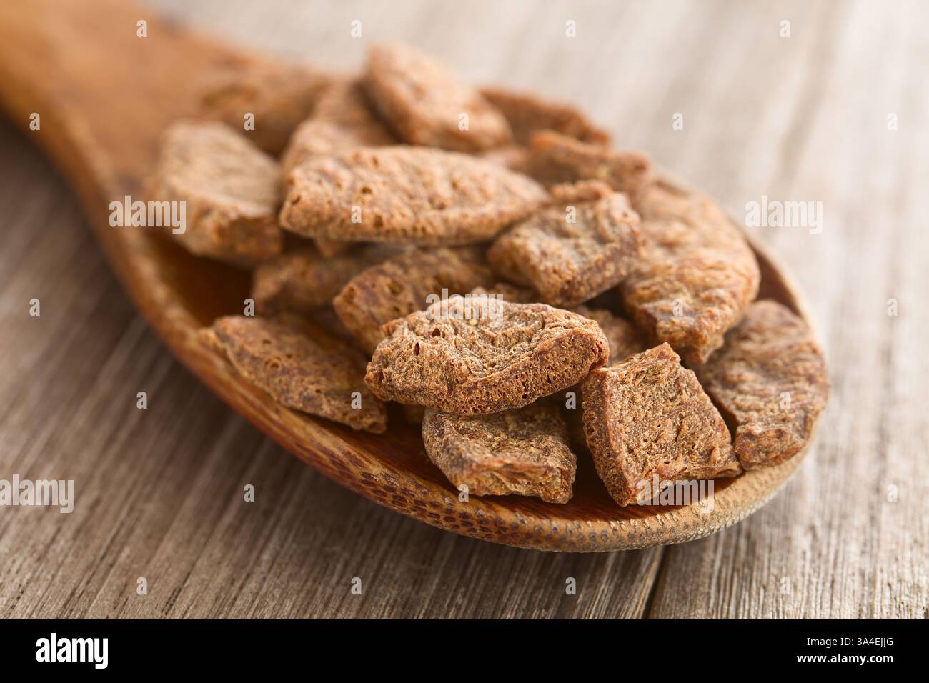 Pezzi disidratati di carne di soia o proteine vegetali testurizzate su cucchiaio di legno (messa a fuoco selettiva, mettere a fuoco un terzo nel cucchiaio) Foto Stock