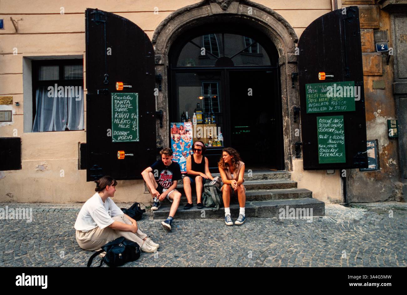 Giovani seduti sui gradini di un bar a Praga. Sono in vendita anche batterie per cibi e bevande. Foto Stock