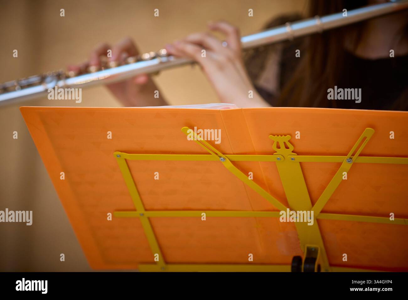 Flautista impegnato a suonare con un supporto musicale arancione e spartiti a fuoco. L'immagine cattura le mani che tengono il flauto, sottolineando l'ex musicale Foto Stock
