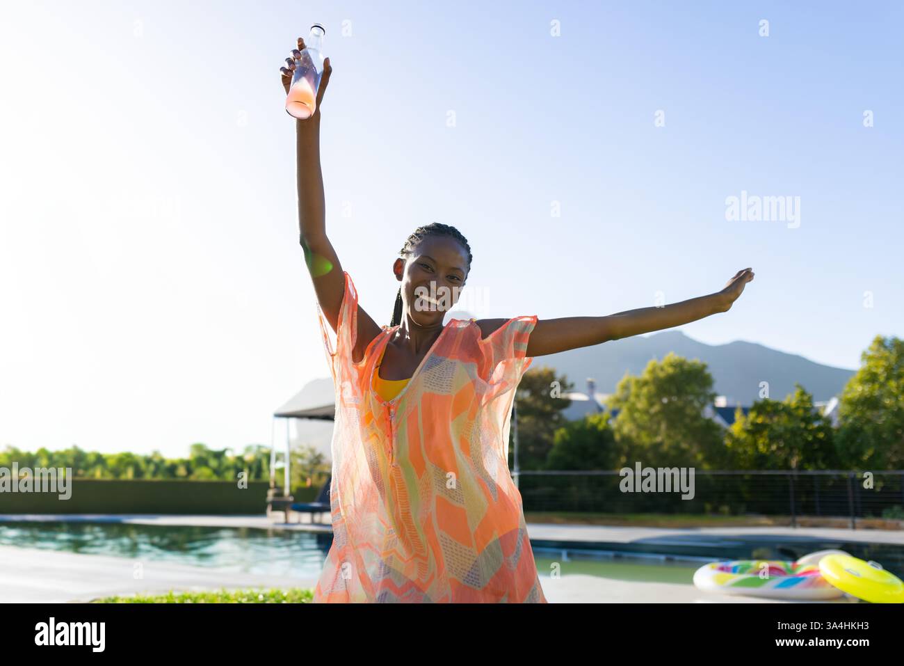 Donna gioiosa in un abito colorato che celebra a bordo piscina, tiene una bevanda rinfrescante e copia spazio Foto Stock Donna gioiosa in un abito colorato che celebra a bordo piscina, tiene una bevanda rinfrescante e copia spazio Foto Stock