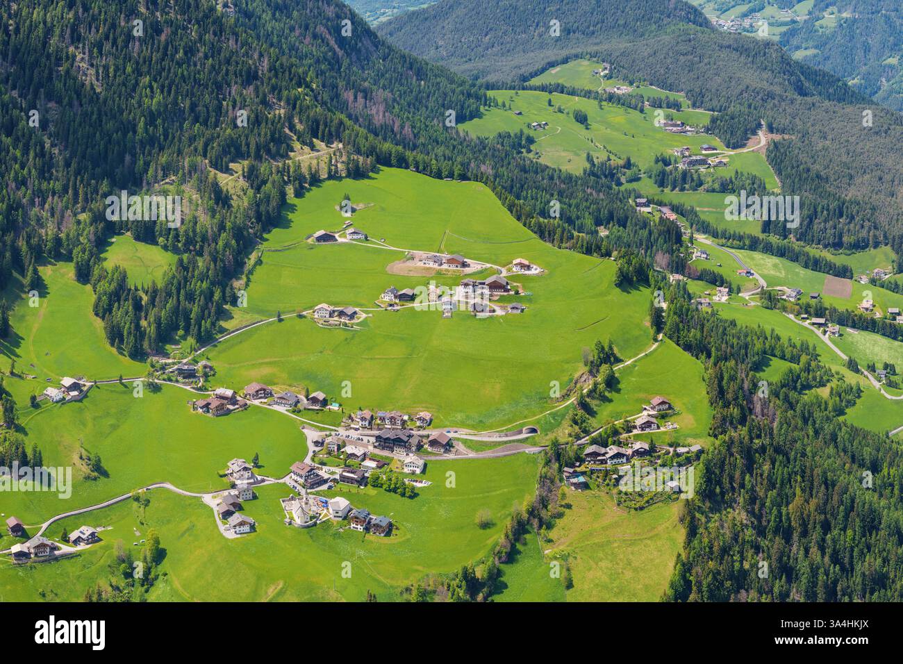 Vista aerea panoramica dell'idilliaco villaggio alpino circondato da lussureggianti colline verdi vicino alla Valle di Funes alle Dolomiti, Italia Foto Stock