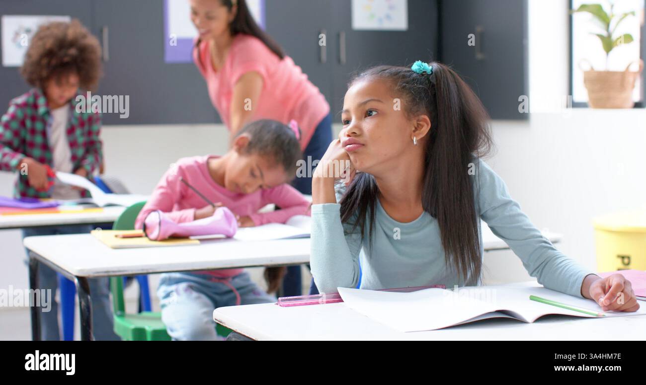 A scuola, ragazza che sogna ad occhi aperti alla scrivania mentre i compagni di classe e l'insegnante lavorano Foto Stock