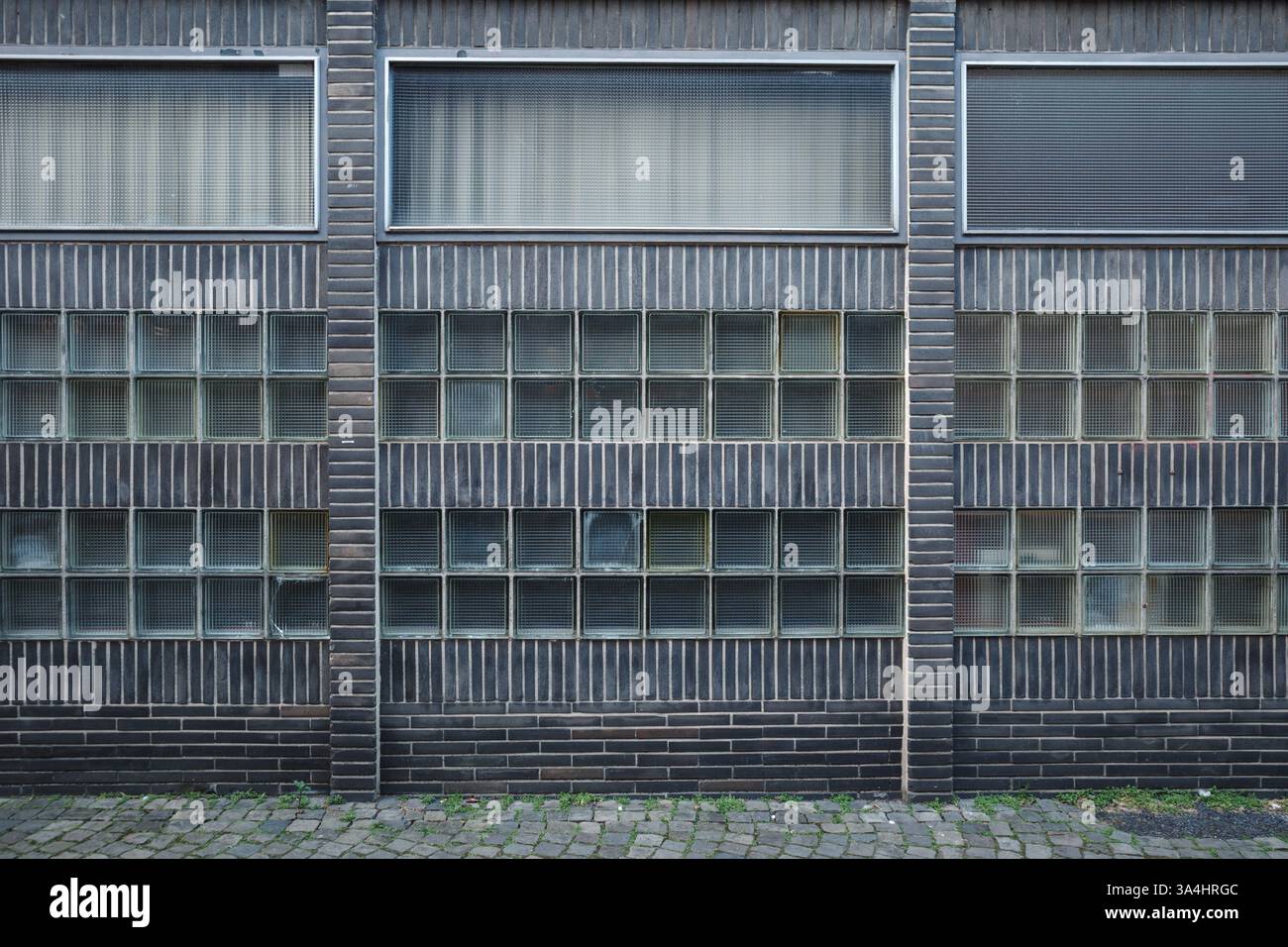 Una facciata di un edificio moderno di stile industriale caratterizzato da mattoni scuri e una griglia strutturata di blocchi di vetro quadrati. Foto Stock