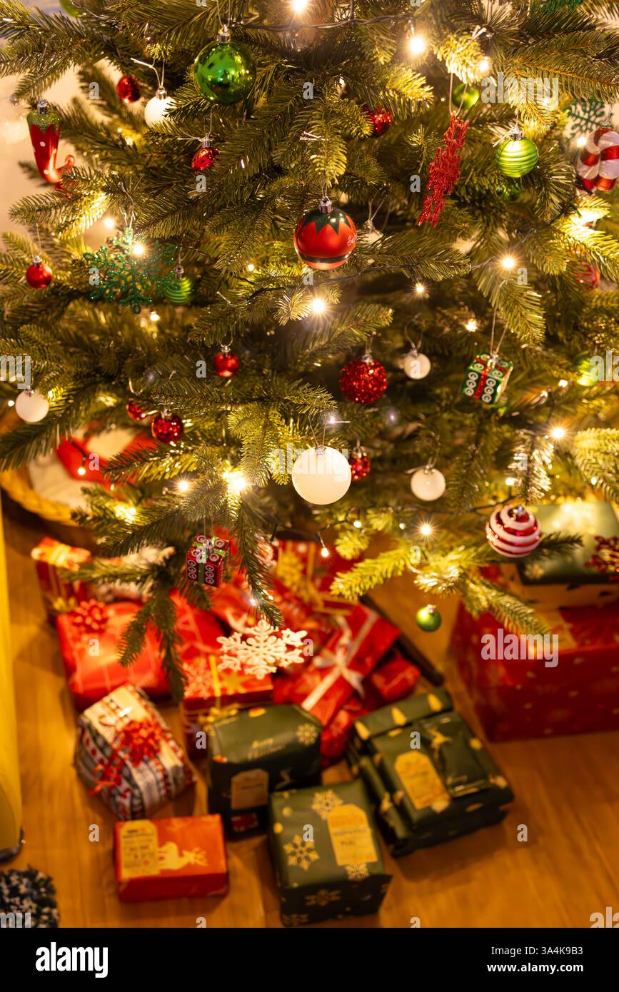 Un'immagine incorniciata verticalmente di un albero di Natale luminoso adornato con ornamenti festivi e luci scintillanti, circondato da regali ben avvolti. Foto Stock