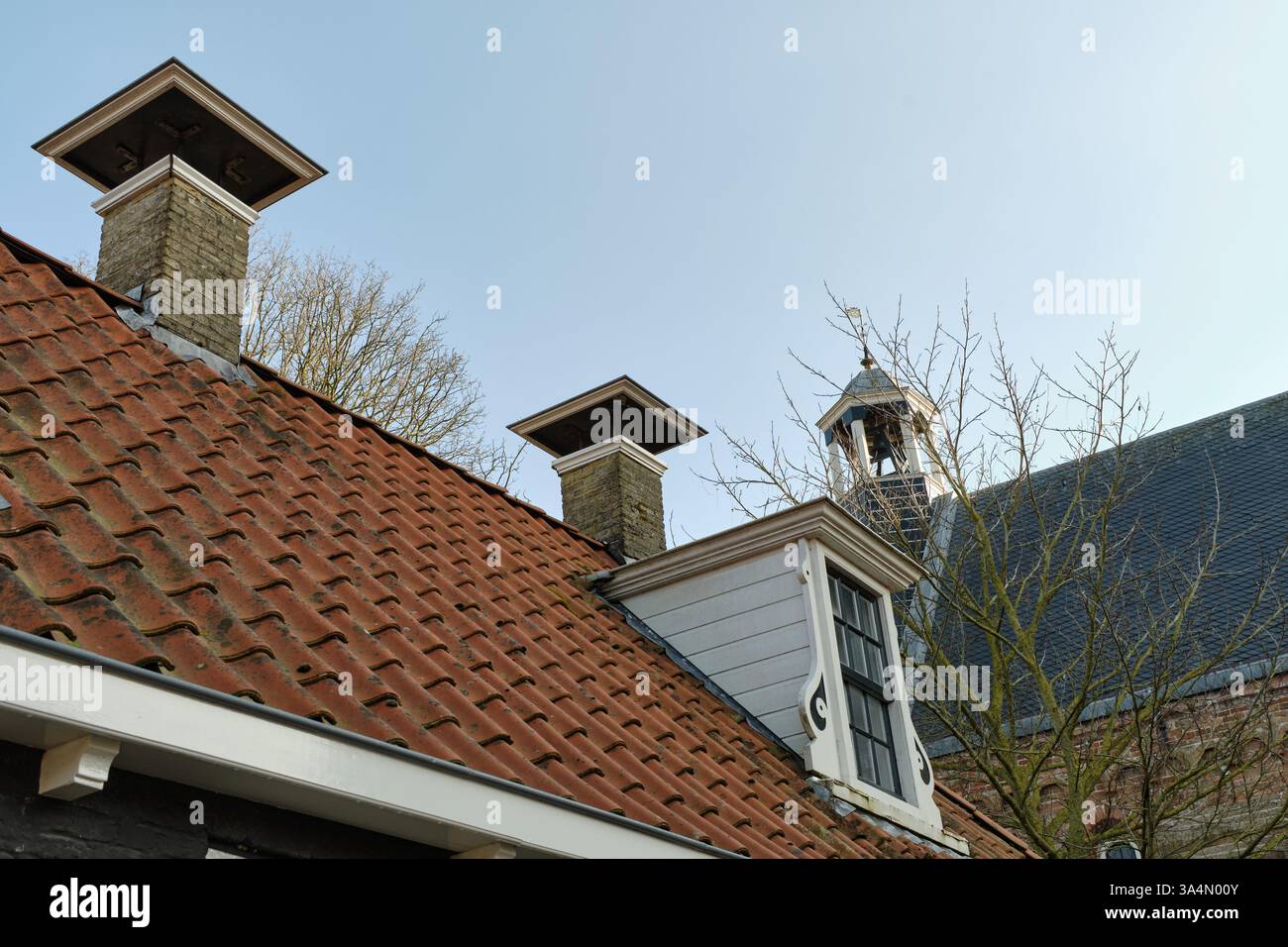 10 marzo 2025 - Grou-Paesi Bassi: Tetti tradizionali con piastrelle di argilla rossa, vecchi camini in mattoni e una finestra dormitorio in un quartiere storico vicino al c Foto Stock