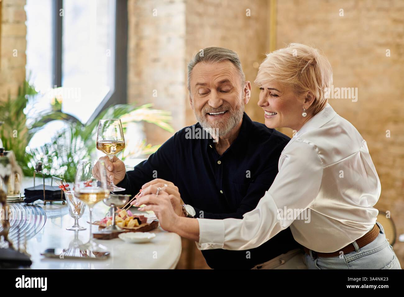 Una coppia matura condivide un momento di gioia con un pasto delizioso adornato da prelibatezze insieme. Foto Stock