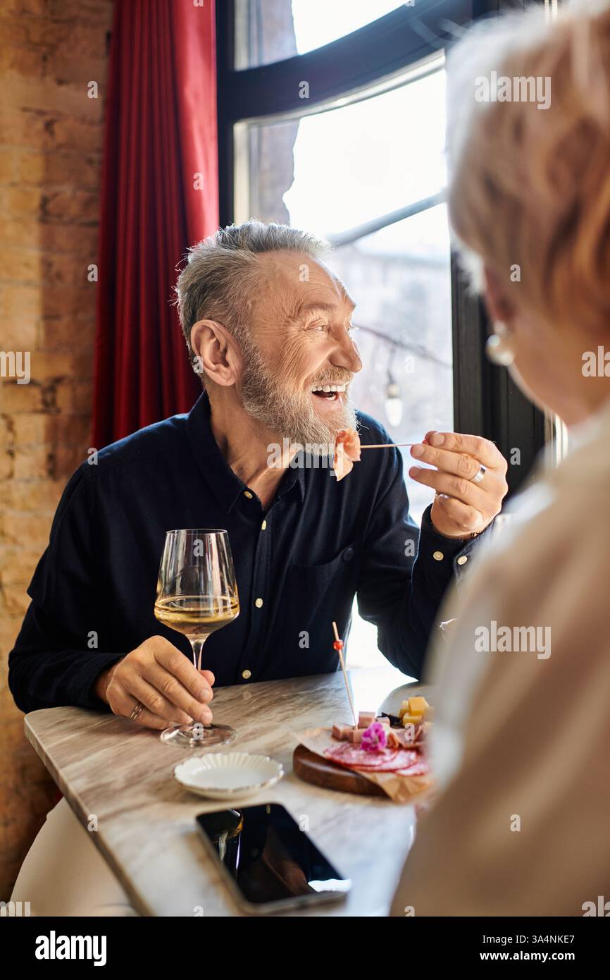Una felice coppia di mezza età si diverte con loro, ridendo di cibo e bevande gustosi. Foto Stock