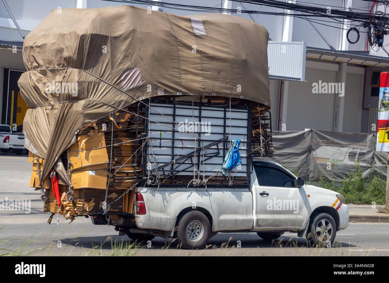 Un pick-up completamente carico di carta per il riciclaggio percorre una strada cittadina, in Thailandia Foto Stock