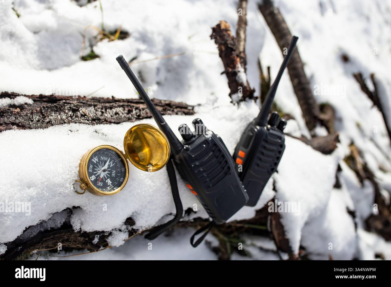 Due walkie talkie neri su un tronco di albero ricoperto di neve bianca ghiacciata accanto a una bussola dorata, gita in montagna Foto Stock
