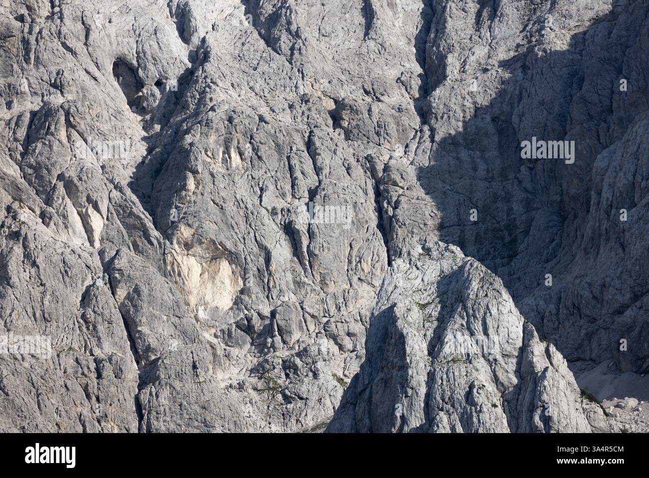 Vista dettagliata di un'aspra parete rocciosa di montagna che mostra texture nitide, fessure e spettacolari ombre naturali. Foto Stock