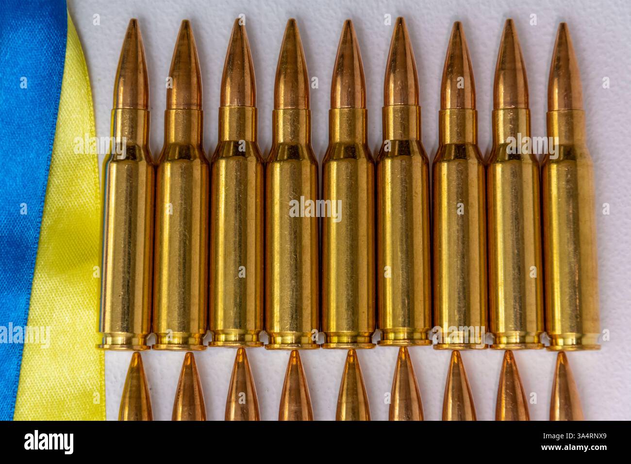 Cartucce di fucile lucide in fila sullo sfondo della bandiera Ucraina. Simbolismo della guerra, delle armi e della resistenza nazionale Foto Stock