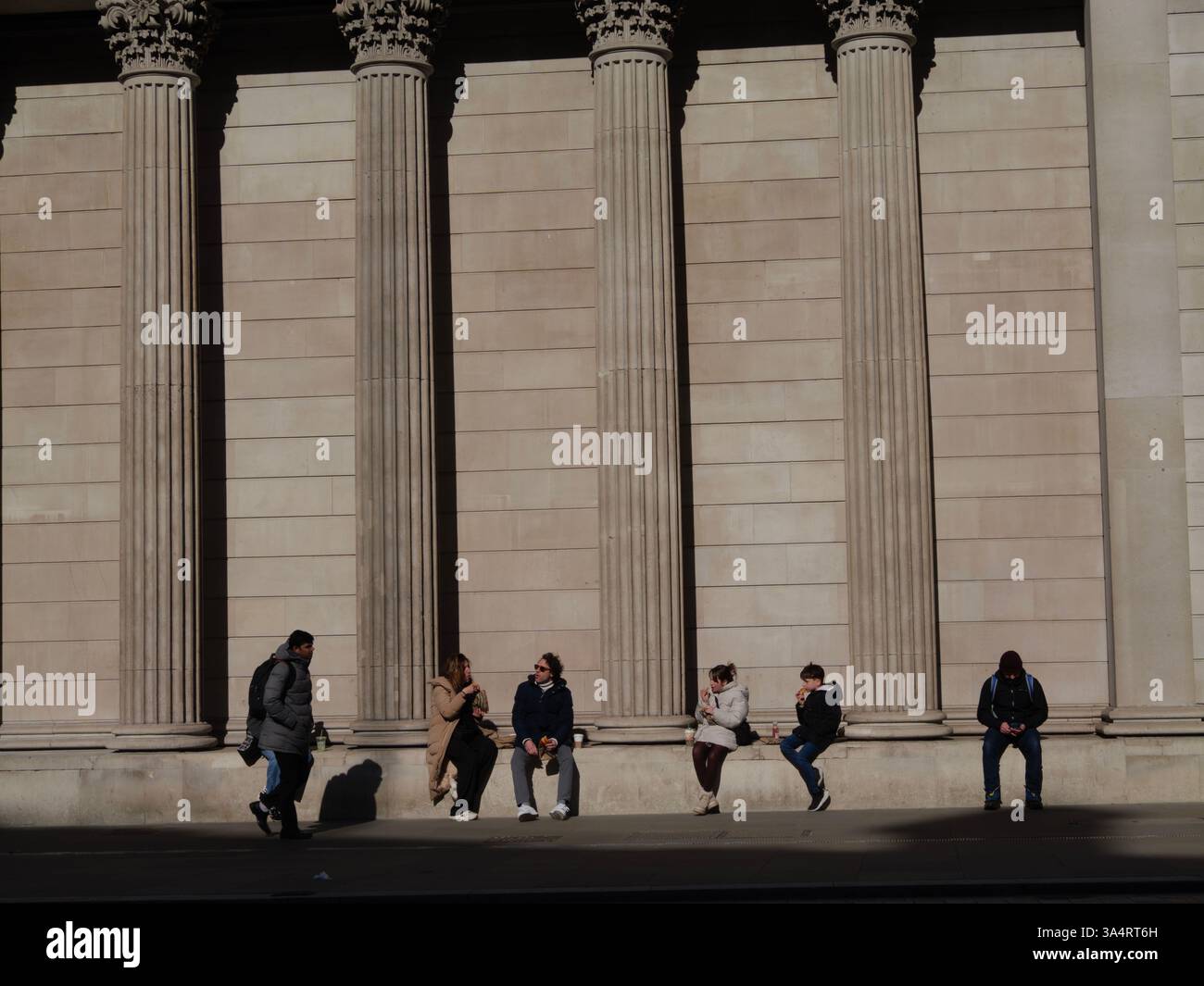 Turisti e lavoratori riposano accanto ai grandi pilastri della Bank of England, Londra, Regno Unito Foto Stock