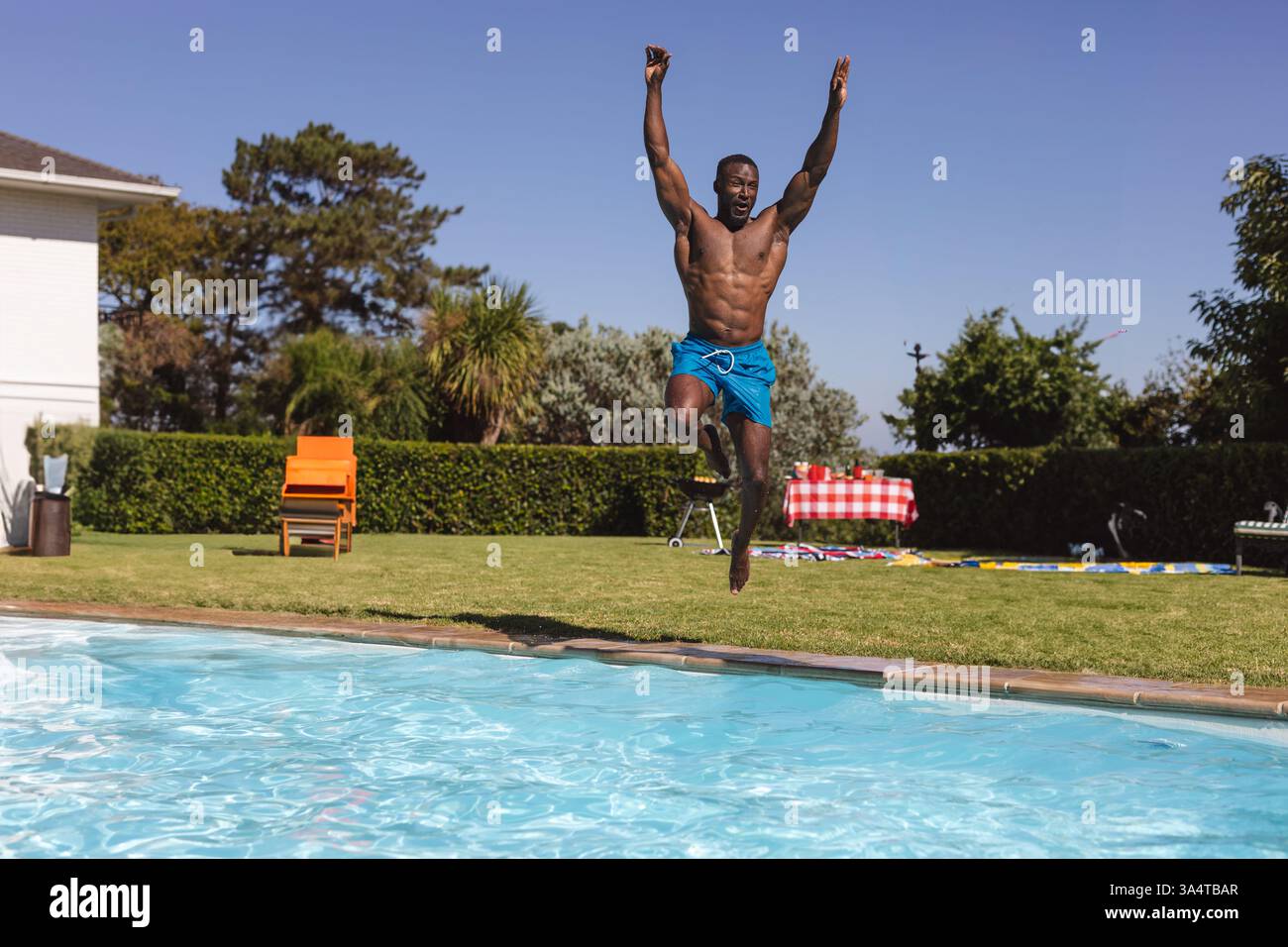 Uomo che si tuffa con gioia in piscina durante la festa in giardino nella giornata di sole, copia spazio Foto Stock