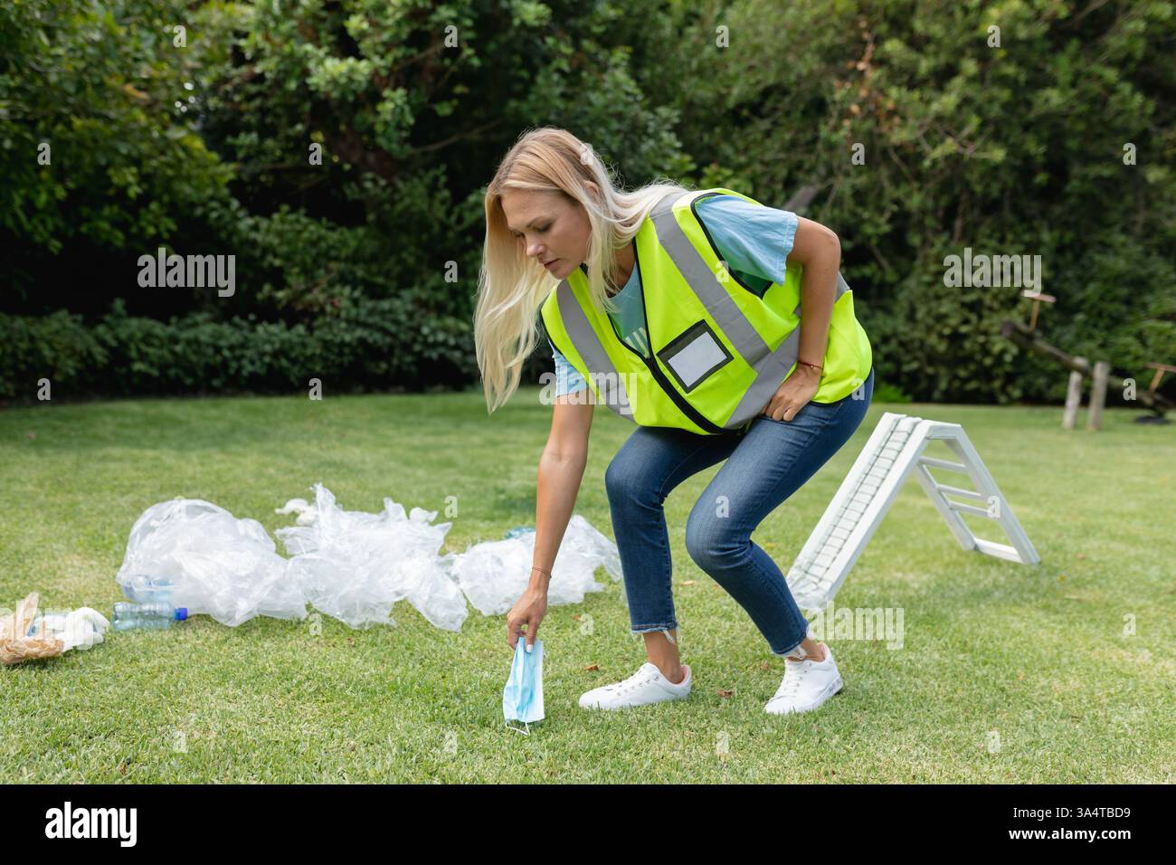 Donna in giubbotto di sicurezza che pulisce i rifiuti nel parco, promuove la tutela dell'ambiente, copia dello spazio Foto Stock