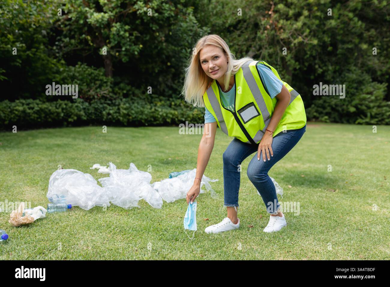 Donna in giubbotto di sicurezza che raccoglie i rifiuti nel parco, promuove la consapevolezza ambientale, copia spazio Foto Stock