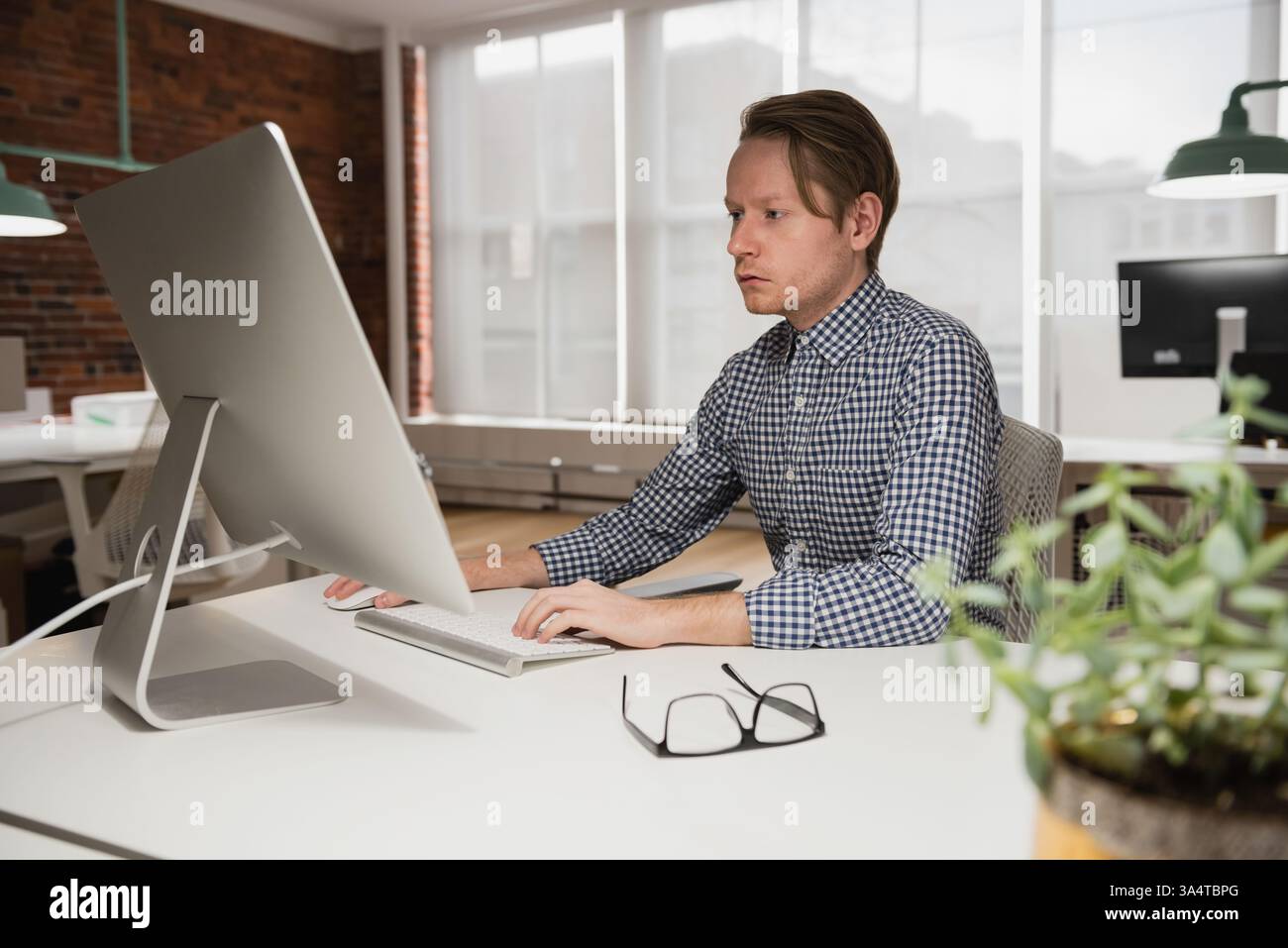 Uomo concentrato che lavora su un computer desktop in un moderno ambiente di ufficio Foto Stock