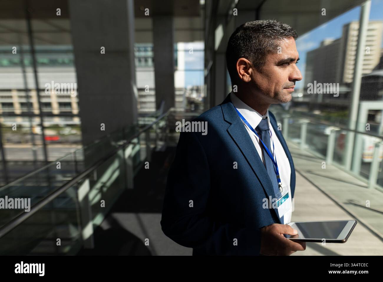 Uomo d'affari con un tablet, in piedi in un moderno edificio per uffici, guardando all'esterno, spazio per copiare Foto Stock