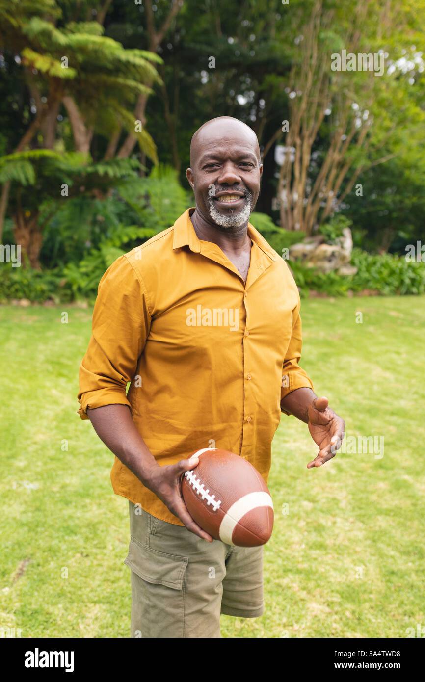 Uomo sorridente che tiene il calcio in cortile, divertendosi all'aria aperta Foto Stock