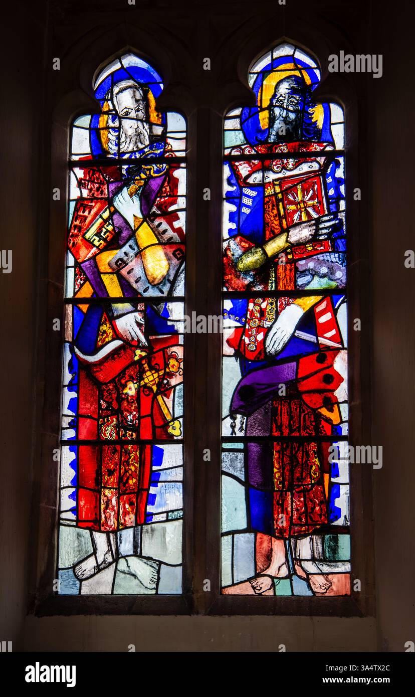 Un paio di vetrate colorate raffiguranti San Pietro e San Paolo in vivaci vesti rosse e blu, ambientate in una chiesa storica. Foto Stock