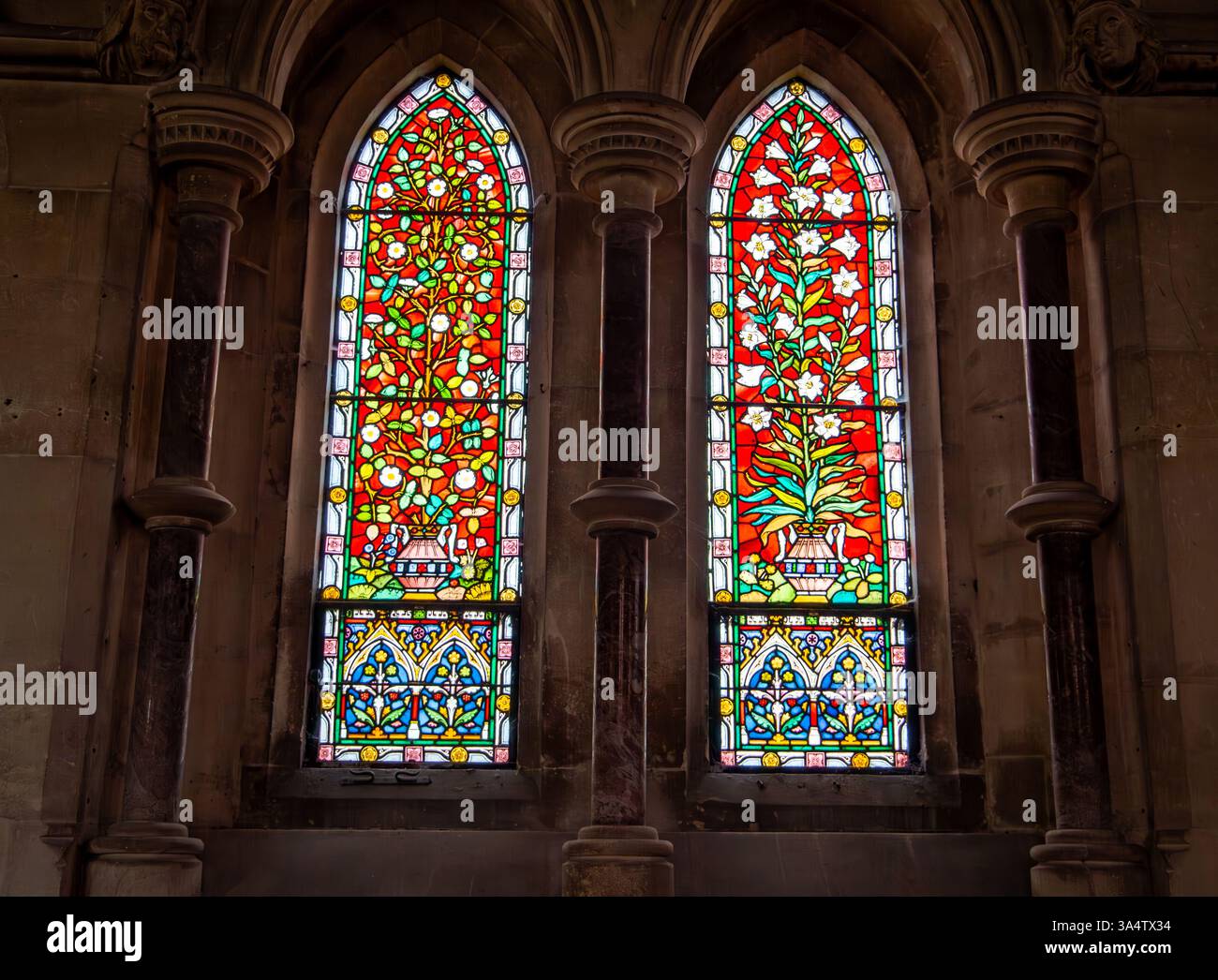 Due vetrate gotiche ornate ad arco caratterizzate da intricati motivi floreali e geometrici in un ambiente storico della chiesa Foto Stock