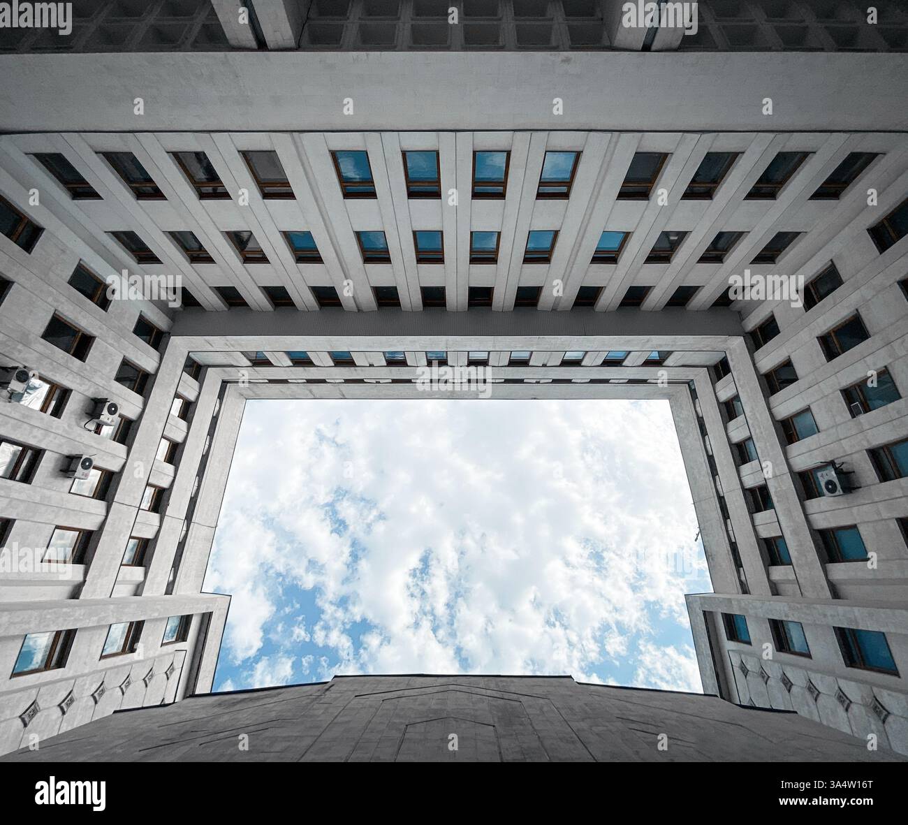 Cortile all'interno di un edificio modernista - affacciato sul cielo. Bene luminoso all'interno dell'edificio per uffici in centro. Facciata con molte finestre. Foto Stock