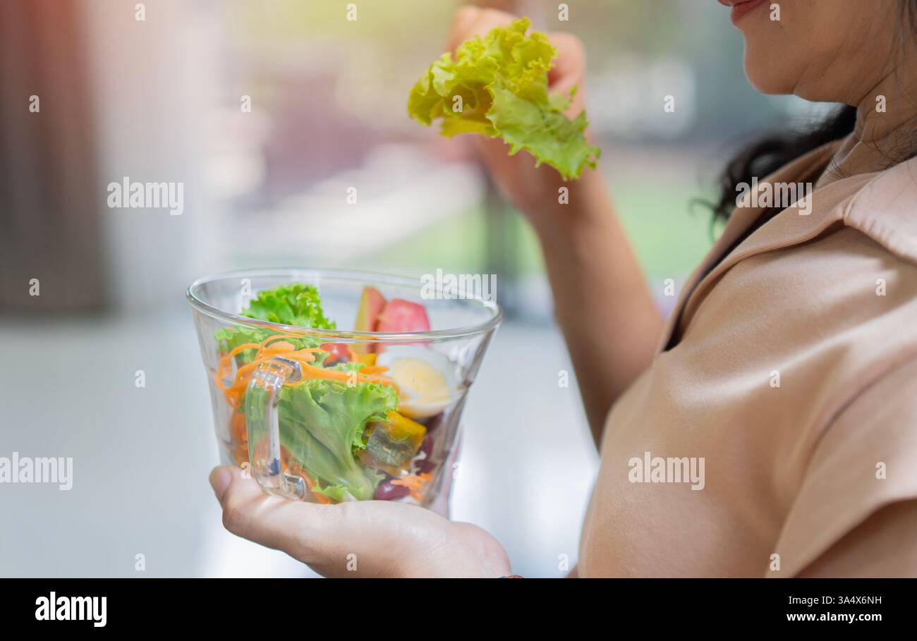 Sana cena vegetariana. Vista laterale della donna seduto sul safa a casa e che tiene la ciotola con insalata fresca. Foto Stock