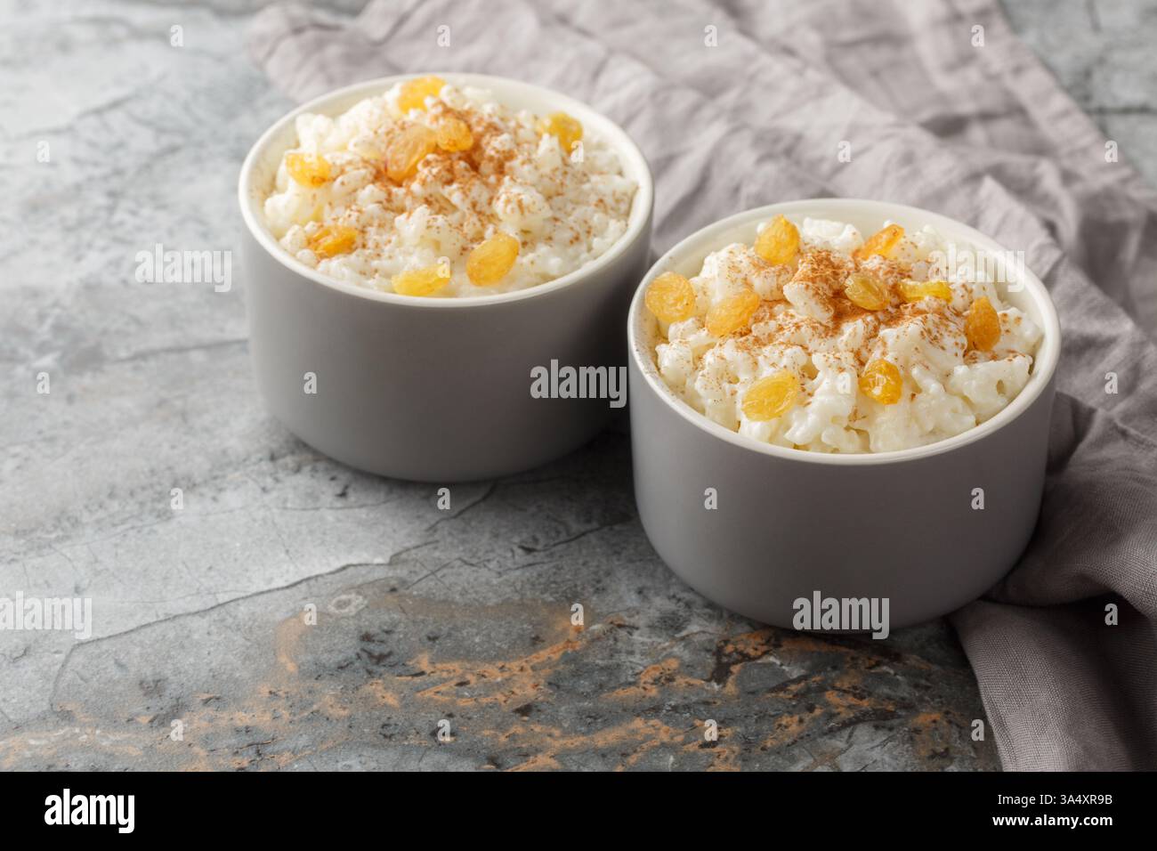 Delicato budino di riso dolce con cannella e uvetta dorata primo piano in ramekin sul tavolo. Orizzontale Foto Stock