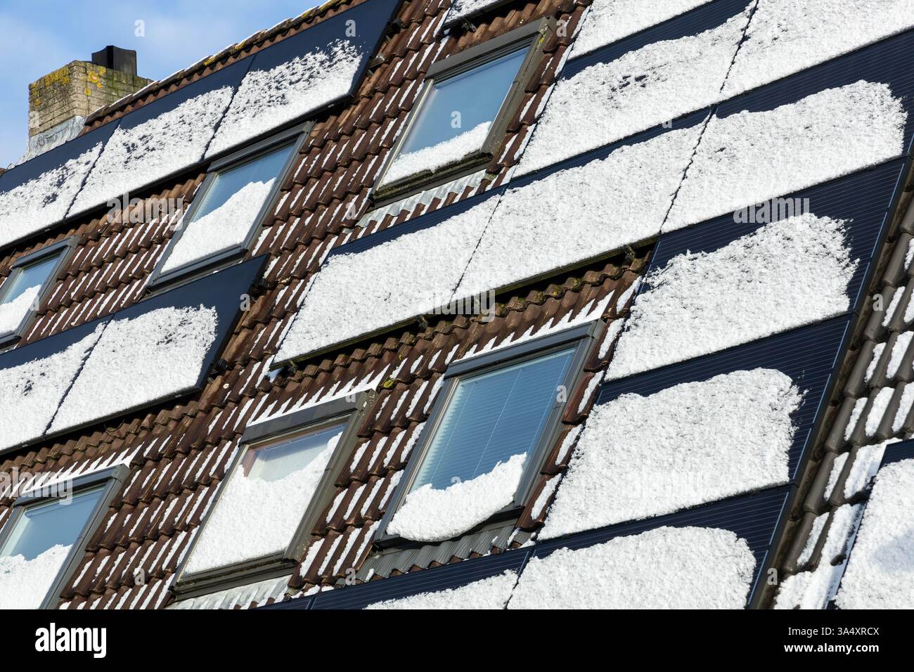 Pannelli solari privati con neve che scioglie sul tetto di una vecchia casa storica e monumentale in inverno. Foto Stock