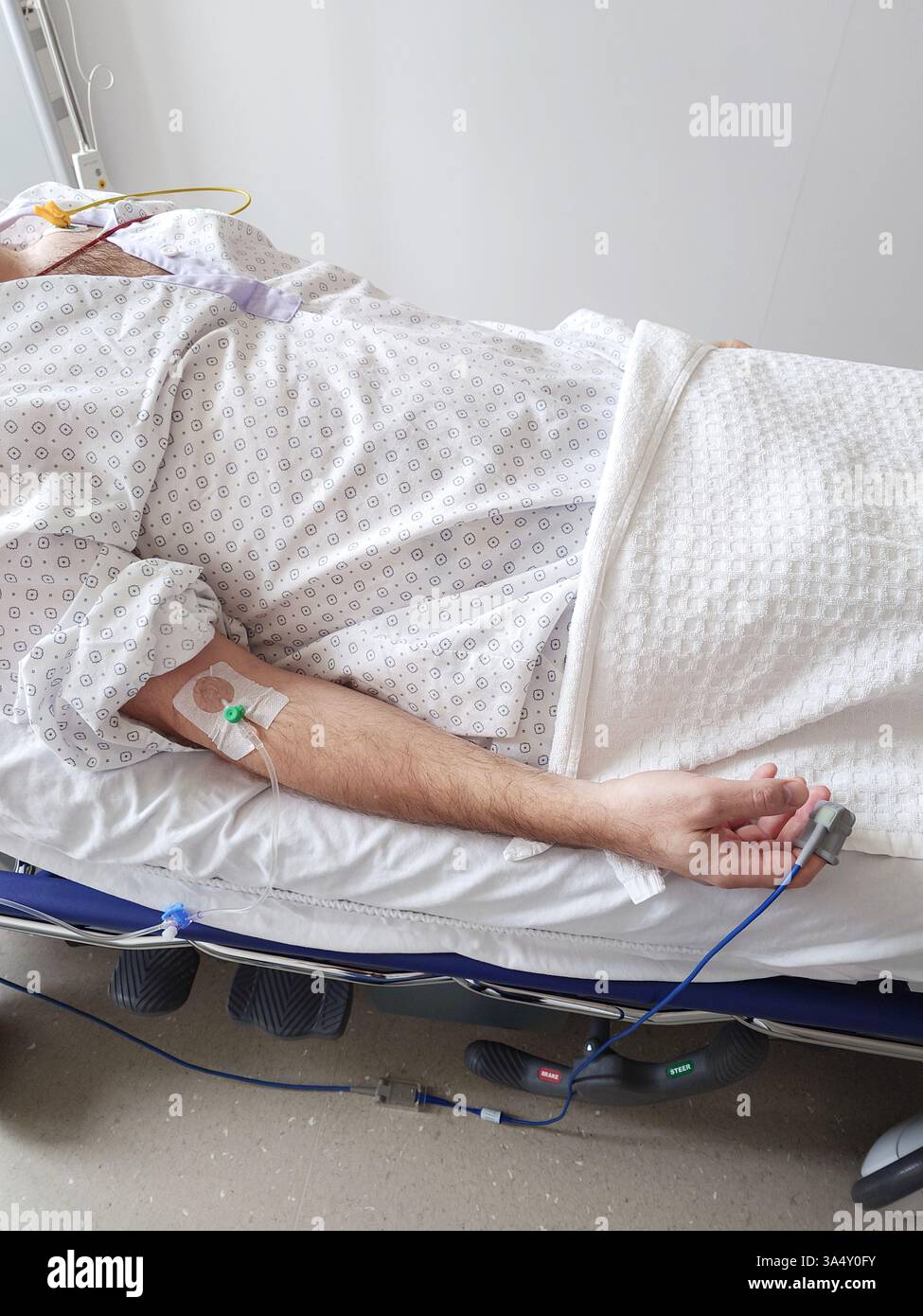 Flebo IV, cannula o branula e pulsossimetro collegato al braccio di un uomo caucasico. Sdraiato in letto d'ospedale, abito paziente medico, primo piano tiro, unrec Foto Stock
