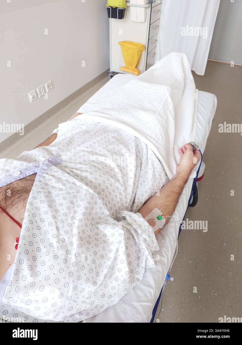 Flebo IV, cannula o branula e pulsossimetro collegato al braccio di un uomo caucasico. Sdraiato in letto d'ospedale, abito paziente medico, primo piano tiro, unrec Foto Stock