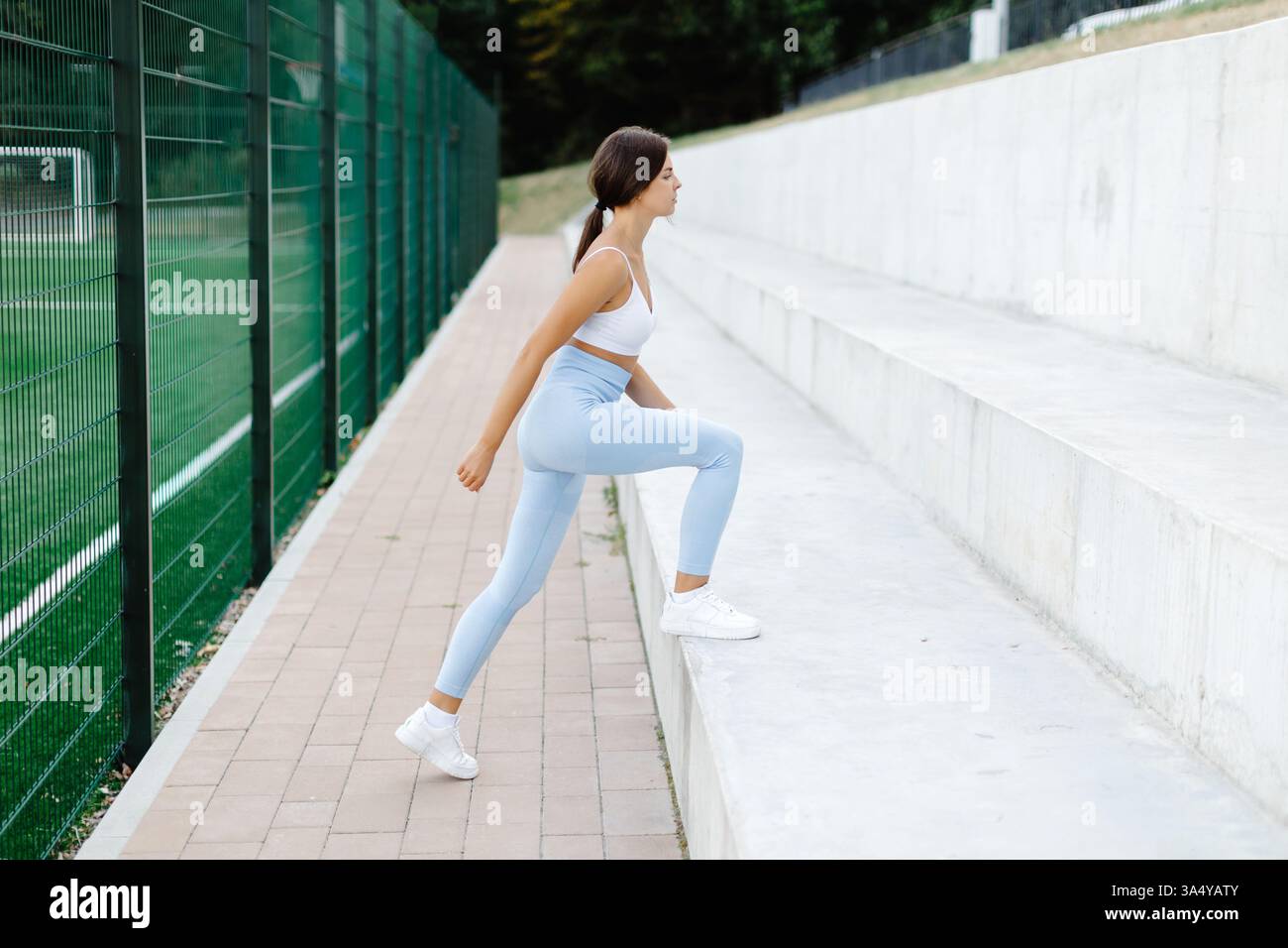 Fit Woman che si allena alle gambe con step-up in una struttura sportiva all'aperto, mostrando dedizione e forza in un ambiente estivo vivace Foto Stock