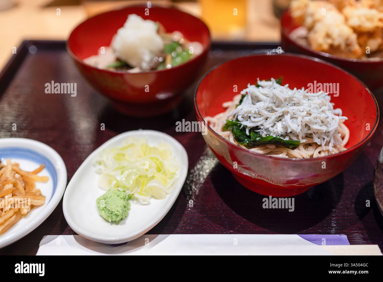 Ciotola di spaghetti soba freddi con pesce fresco di shirasu, accompagnati da condimenti come wasabi e scalpelli. Il piatto fa parte di un ristorante giapponese con Foto Stock