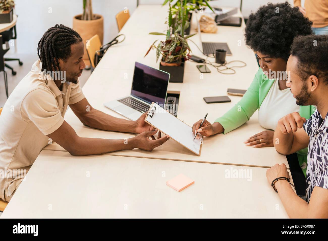 Tre professionisti si impegnano in una discussione di progetto in un ufficio di coworking, condividendo idee su un documento Foto Stock