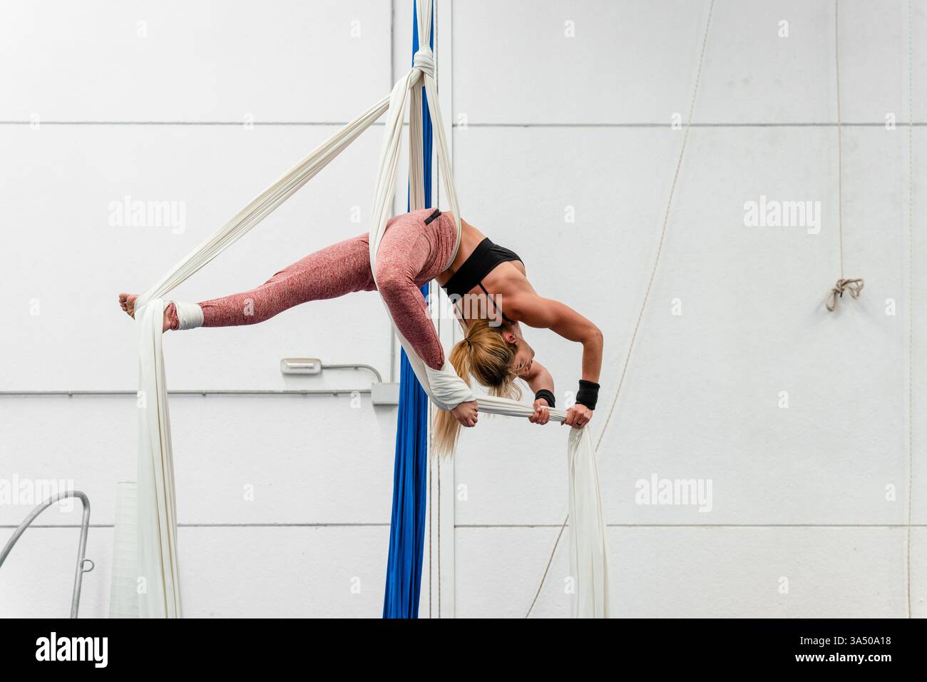 Una donna ispanica esegue sete aeree in una palestra moderna. La scena mostra equilibrio, forza e flessibilità durante una sessione di fitness al chiuso. Foto Stock