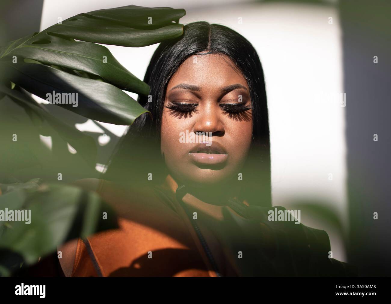 Un modello afro-americano di dimensioni più grandi si trova all'interno, guardando avanti con un'espressione premurosa. Il ritratto enfatizza la sicurezza, la positività del corpo e un ambiente interno moderno. Foto Stock