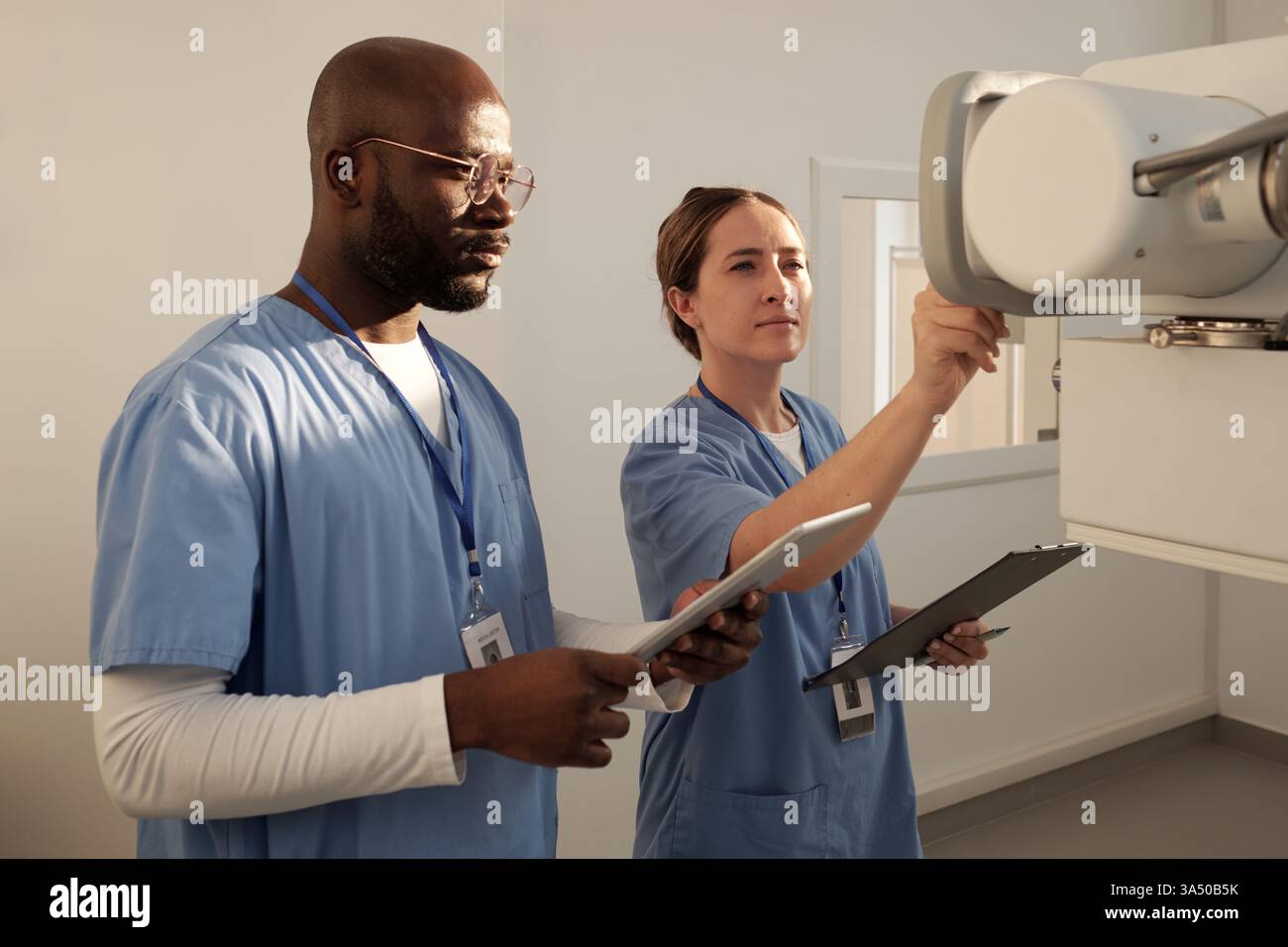 Due giovani medici in uniforme accendono le apparecchiature mediche in ambiente ospedaliero. La scena mette in evidenza il lavoro di squadra e l'assistenza sanitaria moderna in azione. Adatto per ospedale, clinica e campagne di marketing di assistenza sanitaria. Foto Stock