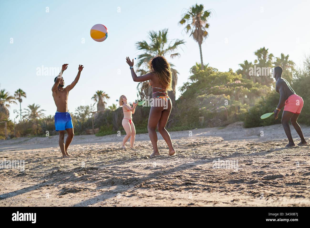 Tiro ad angolo basso di un gruppo eterogeneo che lancia una palla e gioca a Beach tennis su una spiaggia soleggiata. Trascorrono un vivace weekend estivo al mare. Perfetto per viaggi, attività ricreative e immagini di stili di vita multietnici. Foto Stock