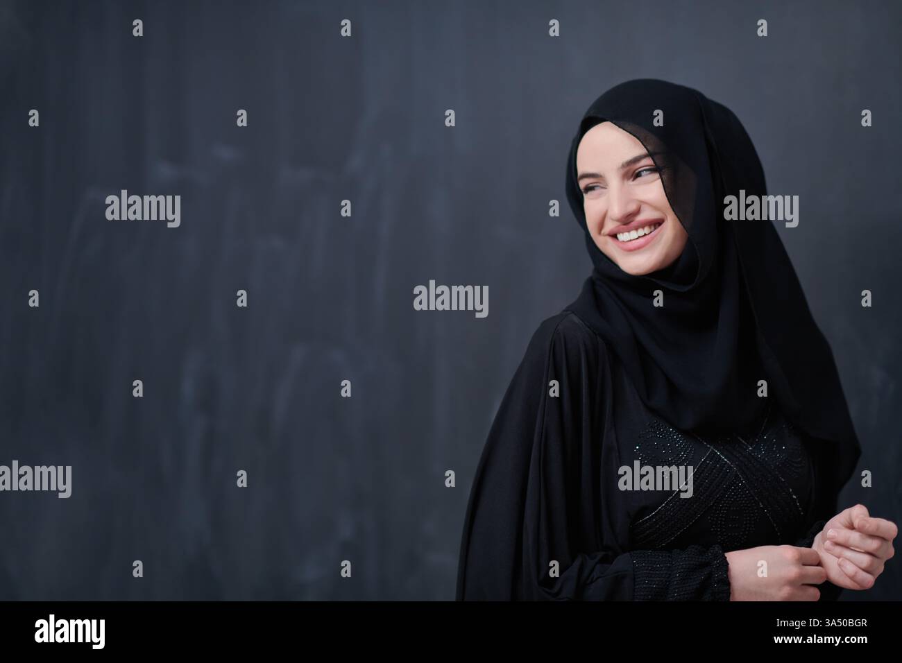 Ritratto di un'elegante donna musulmana che indossa un hijab davanti a una lavagna nera. La scena comunica la moda islamica moderna, il Ramadan Kareem e lo stile culturale. Ideale per campagne di moda, fede e Ramadan, editoriali o e-commerce. Foto Stock