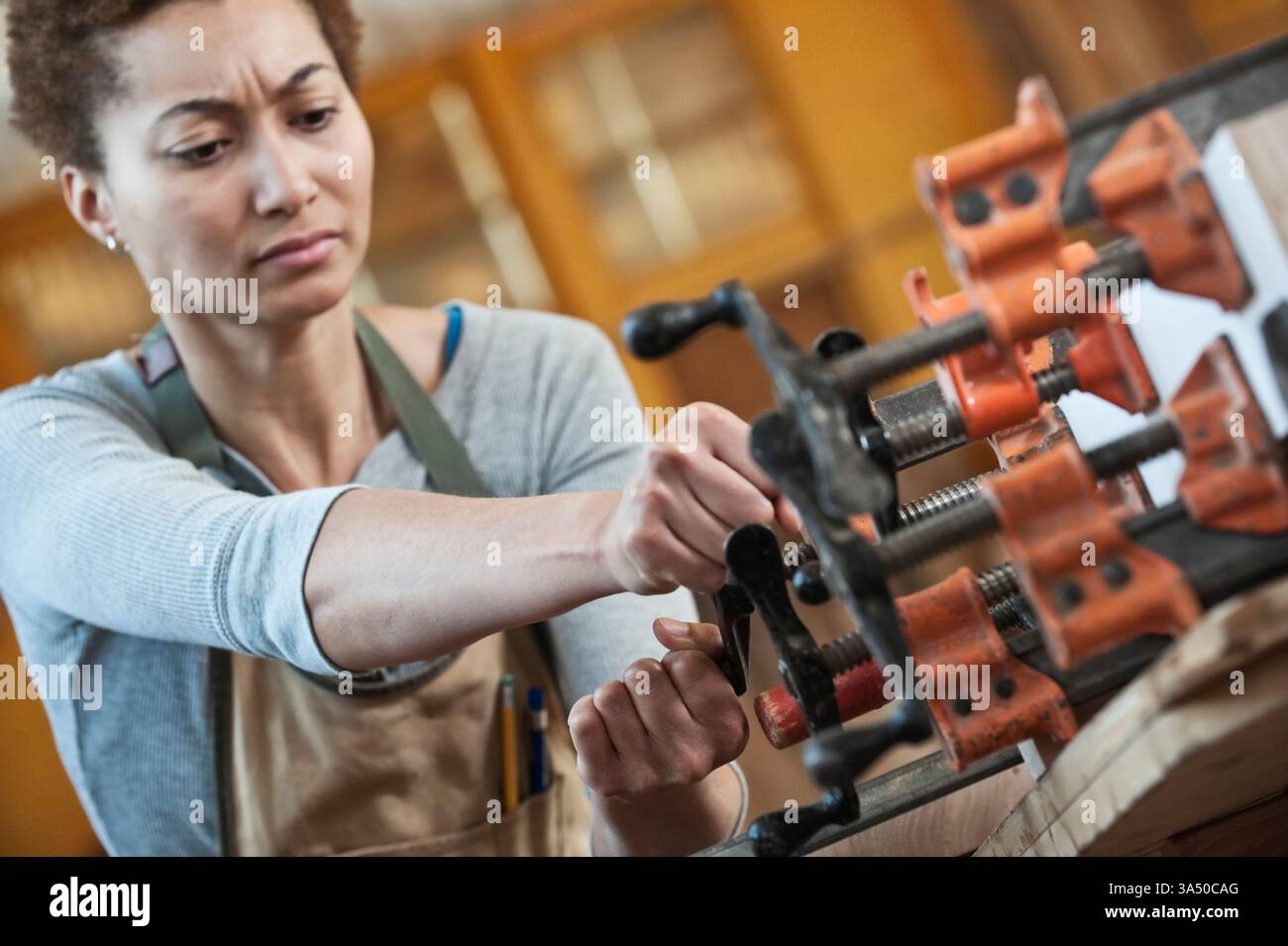 Ritratto di una falegnameria nera in un'officina di lavorazione del legno, che regola i morsetti mentre si lavora con il legno. Mette in evidenza i mestieri specializzati, le donne professionisti e le carriere nei colletti blu in ambito edile. Ideale per campagne che promuovono le donne nei mestieri, nell'artigianato e nell'edilizia sostenibile. Foto Stock